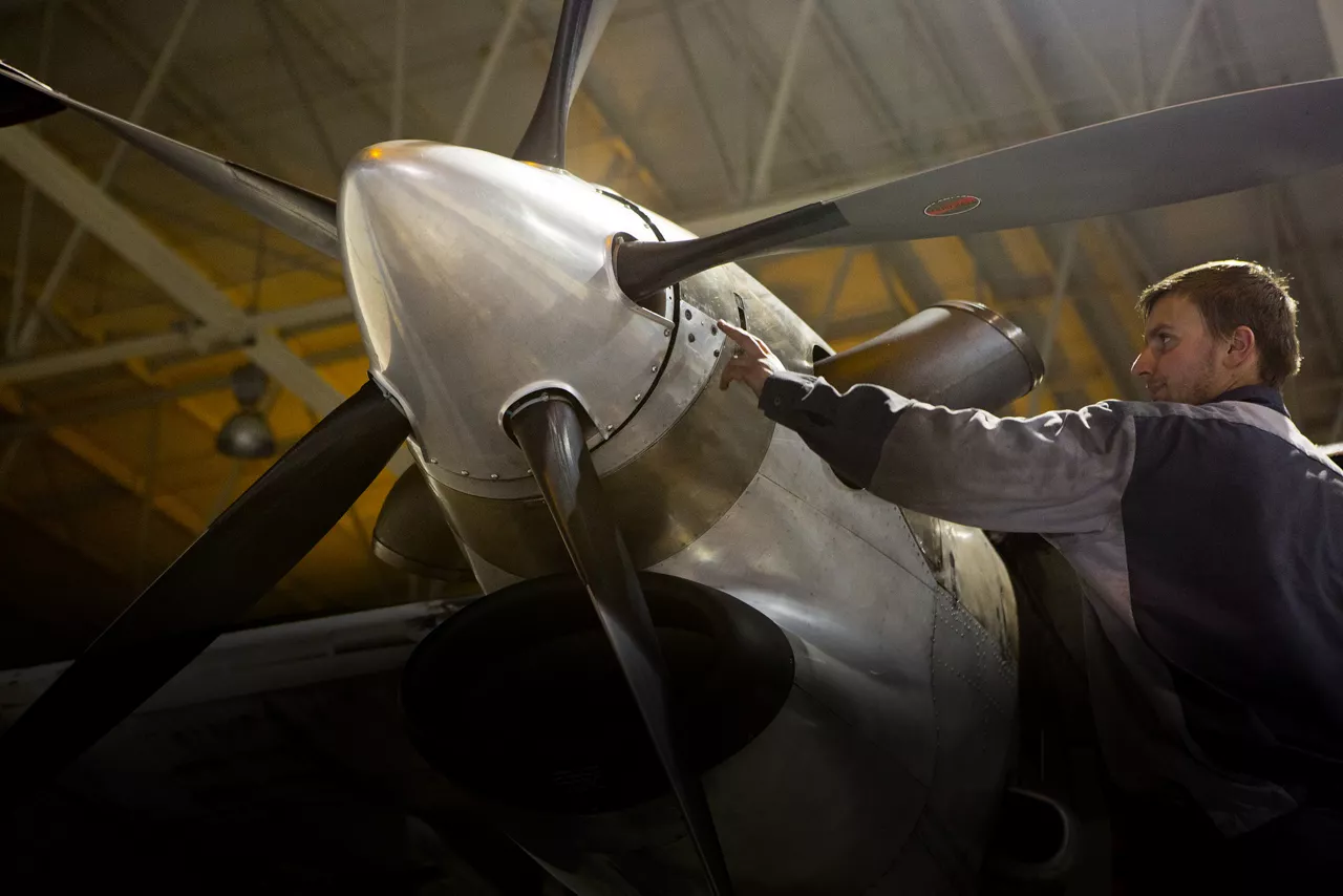 A pilot works on an airplane in a dimly lit hangar