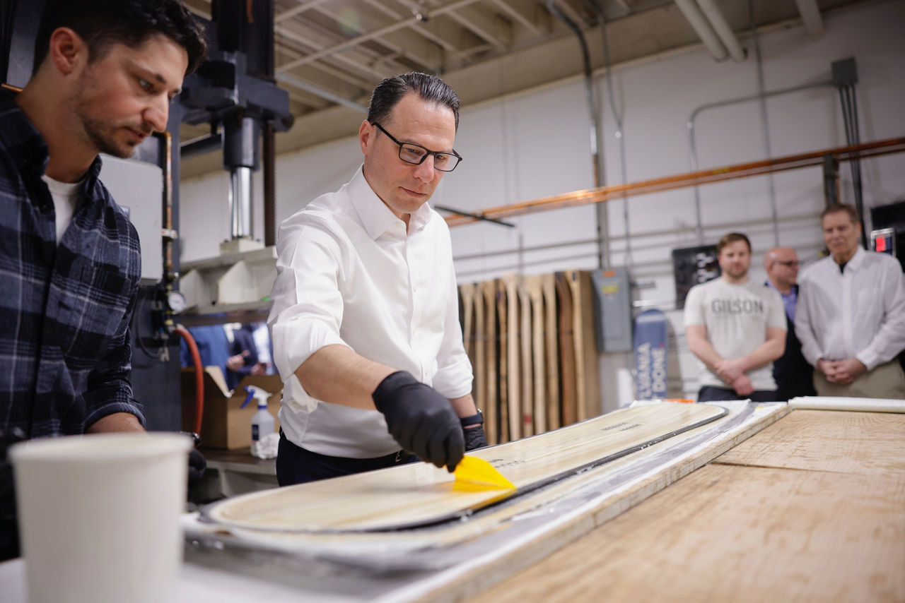 PA Governor Josh Shapiro spreads wax on a made in PA snowboard. 