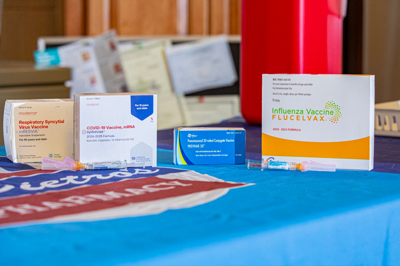 Four boxes and syringes of different immunizations, including RSV, COVID-19, pneumonia, and flu