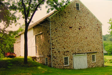 Two-story stone barn with steep gable roof and ramped side entrance and gable end entrance.