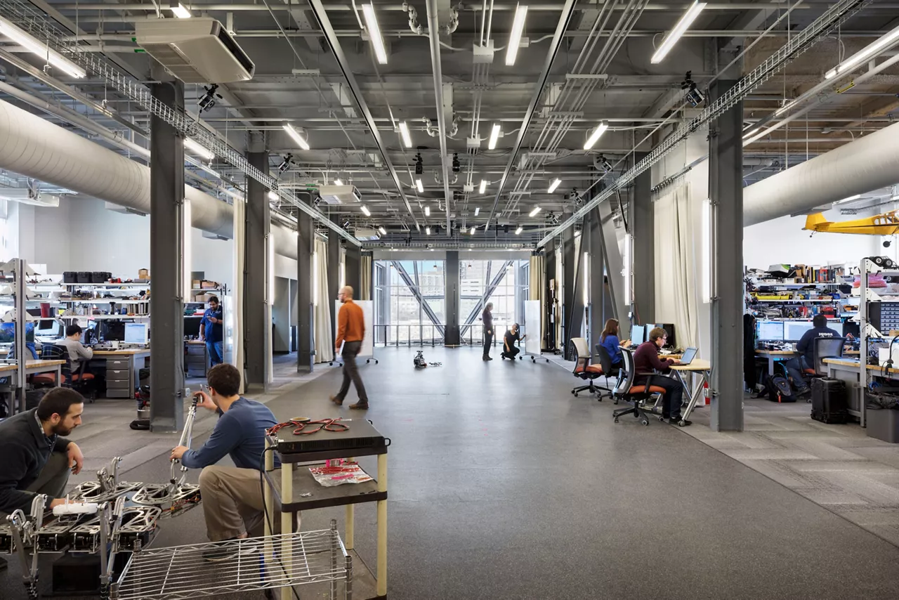 An industrial, modern office space with a few people mingling in the background