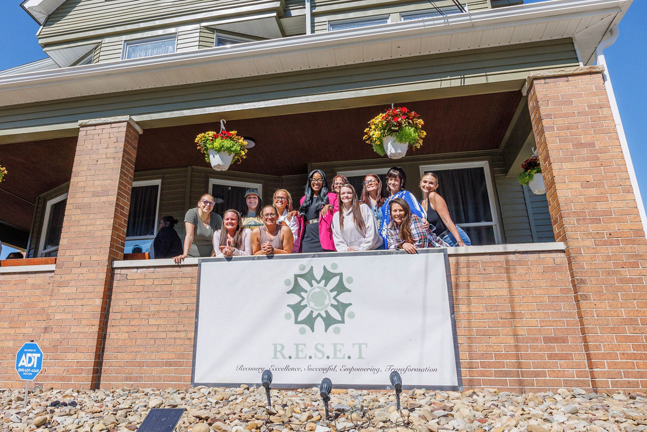 Secretary Dr. Latika Davis-Jones stands with RESET BC staff and clients on the porch of the Beaver County halfway house for women. A sign in front of the house reads, “R.E.S.E.T. — Recovery, Excellence, Successful, Empowering, Transformation.”