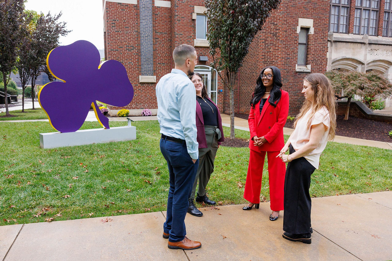 Pennsylvania Department of Drug and Alcohol Programs Secretary Dr. Latika Davis-Jones speaks with current students and alumni outdoors on Carlow University's campus in Pittsburgh, near the university's shamrock sculpture.