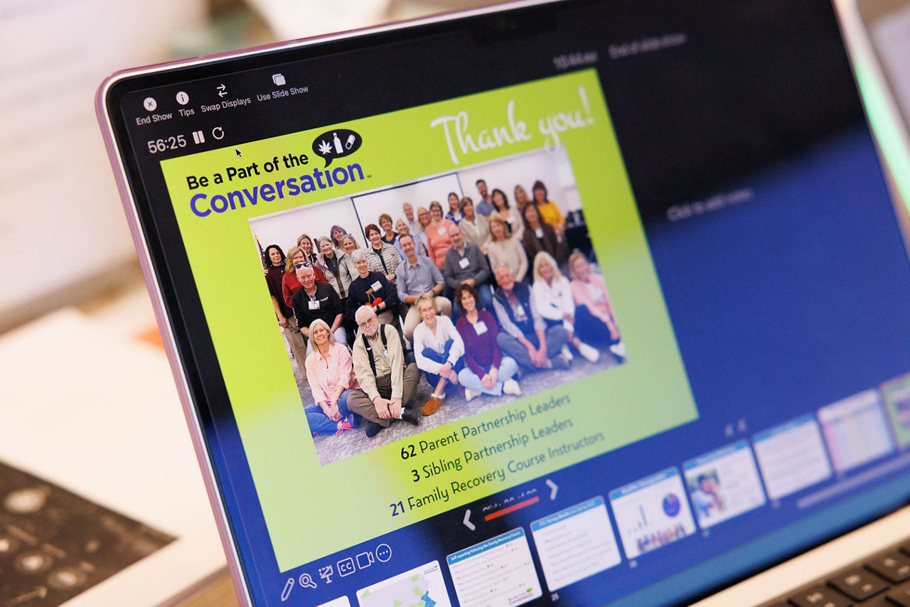 A laptop screen displays a Be a Part of the Conversation presentation slide thanking 62 Parent Partnership Leaders, three Sibling Partnership Leaders, and 21 Family Recovery Course instructors.