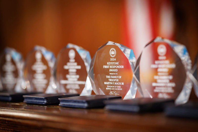 Glass awards lined up in a row. One award in focus reads: 2024 Keystone First Responder Award. Presented to the family of Trooper Martin F. Mack III.