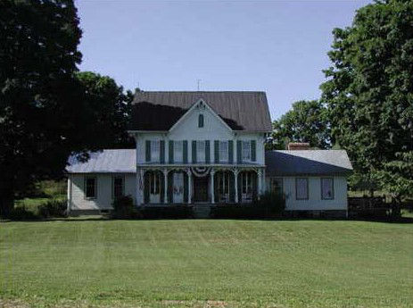 5-bay white farmhouse with steep side- gabled roof and front facing gable and a decorative front porch with turned posts.