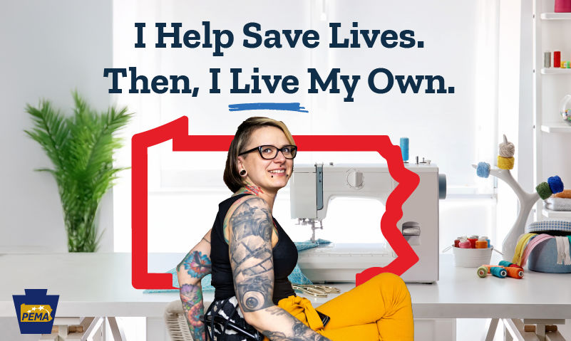 911 dispatcher Lisa sits in a call center and smiles while looking off camera. She has blue eyes and long gray hair, and is wearing a red, white, and blue patterned shirt.