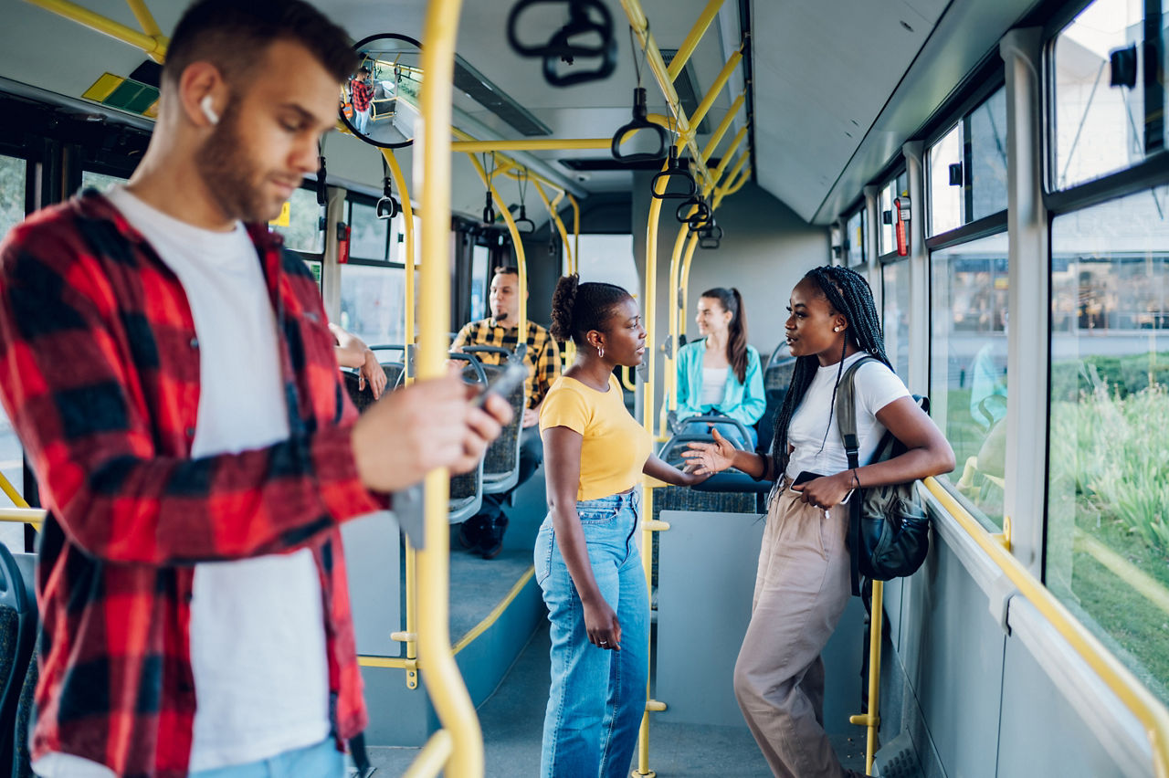 Two young african american female friends standing in a moving bus and talking cheerfully. Two black woman commuting in a public transport. Best friends traveling together in a city