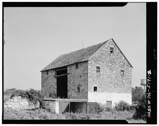 Front view of three-level stone barn with a steeply gabled roof.