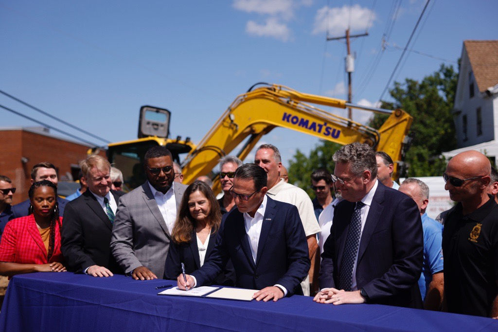 Governor Shapiro signing a bill in front of a crowd with a construction digger.