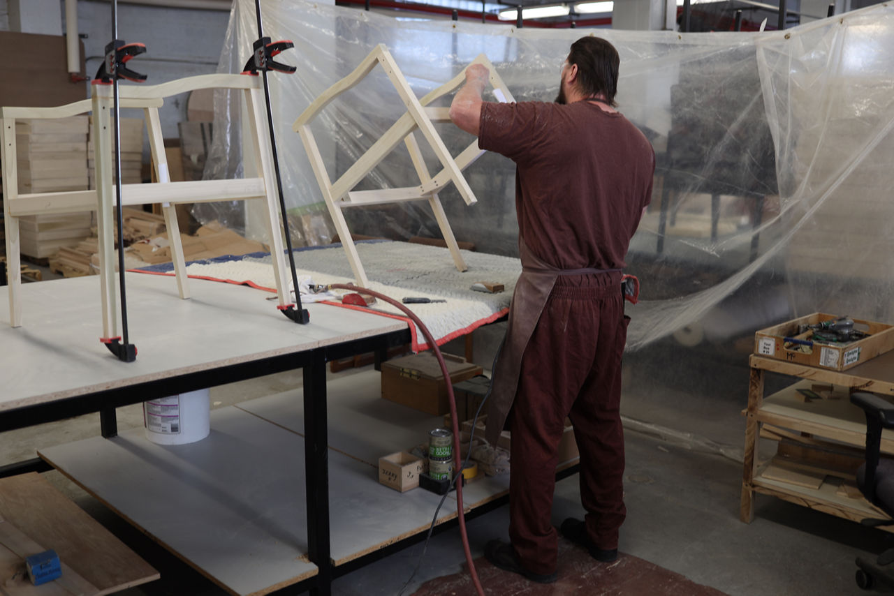 An incarcerated individual sands the wooden frame of a chair.