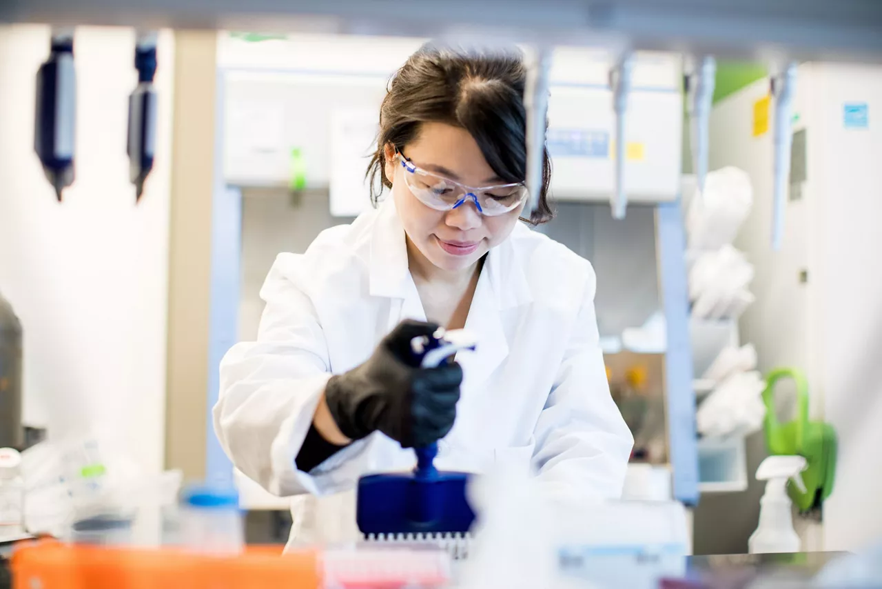 A scientist wearing a labcoat and safety goggles works in a clean room lab space