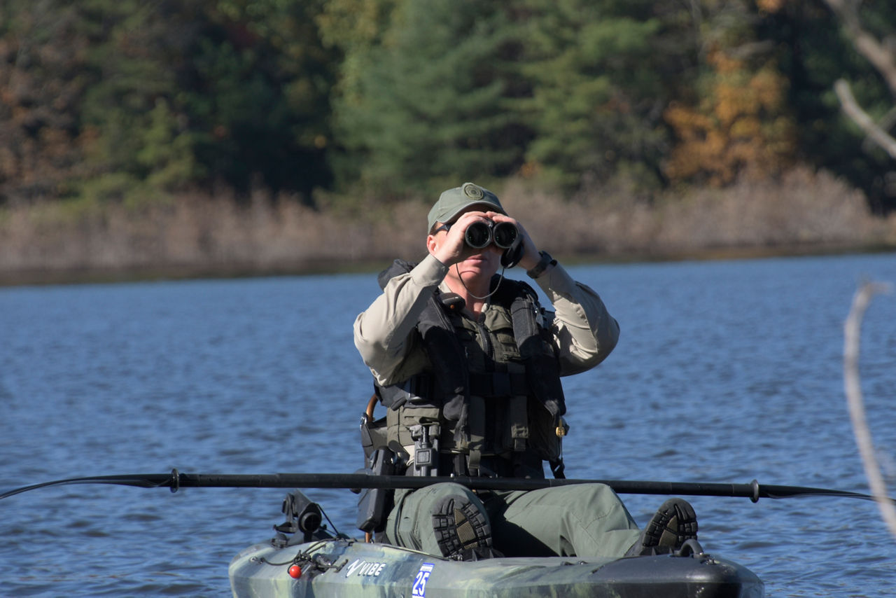 Waterways Conservation Officer on a waterway in a kayak looking through binoculars