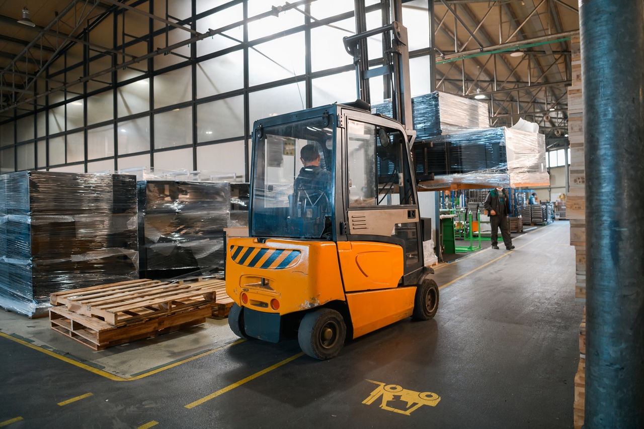 A forklift carrying a pallet of goods drives through a distribution warehouse