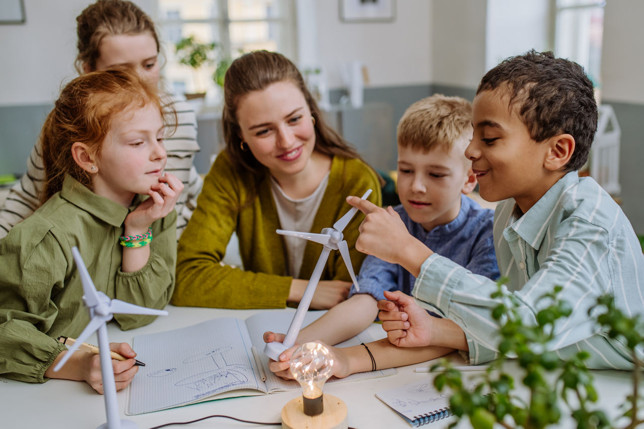 Young teacher with model of wind turbine learning pupils about wind energy.
