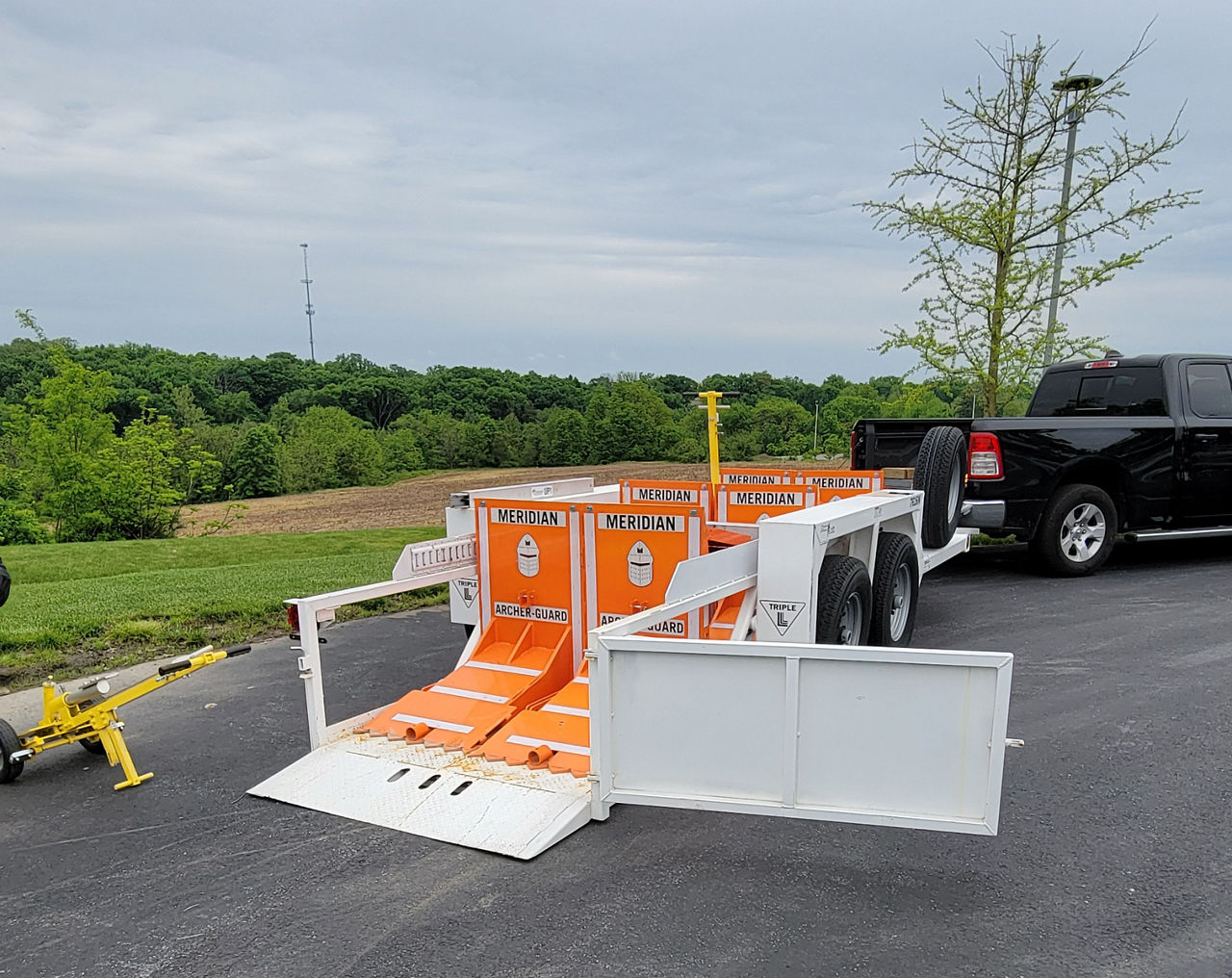 Image of a black truck hauling a white trailer with orange barriers loaded onto it.