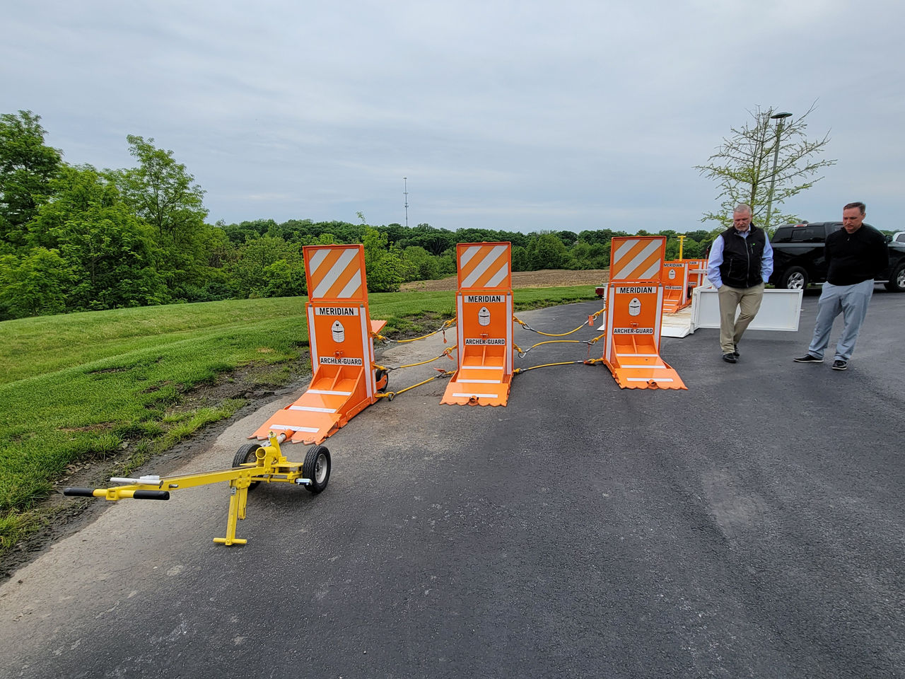 Image of three connected orange mobile barriers set up side-by-side while two men demonstrate the mobile barrier system.