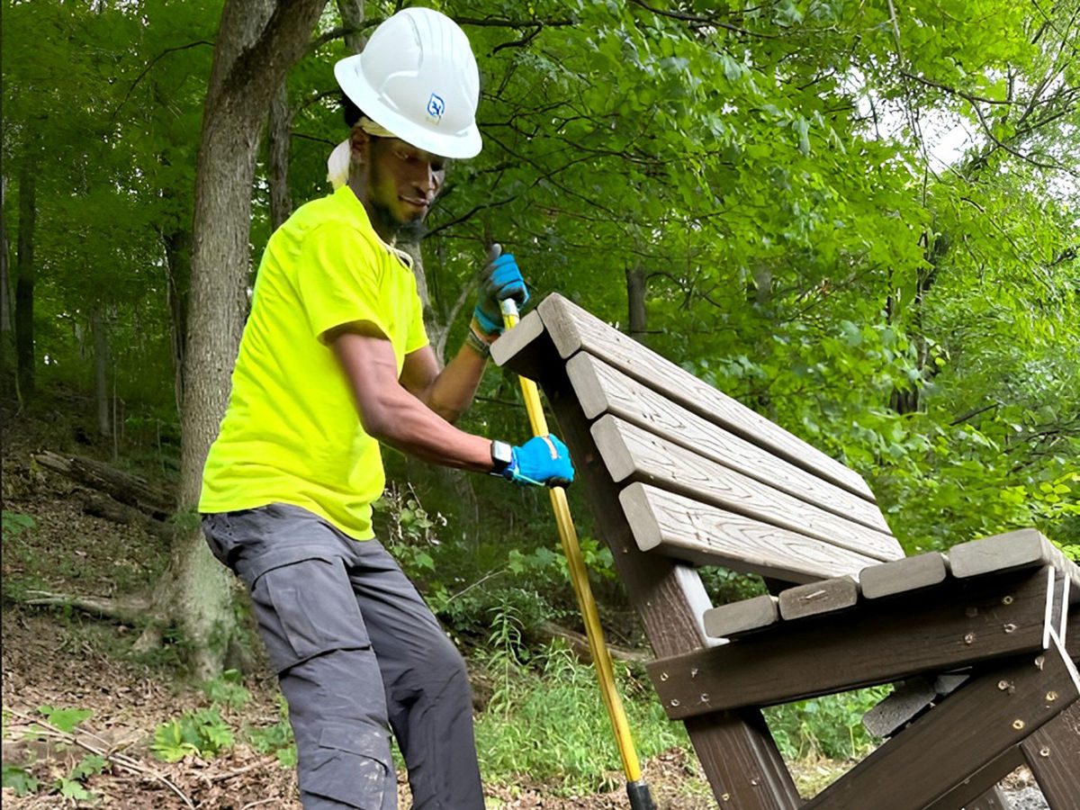 An Outdoor Corps member helps install a bench using a handled tool.