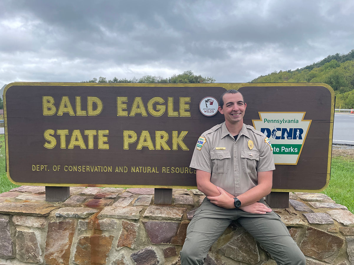 Assistant Park Manager Ty Moon sits in front of the Bald Eagle State Park sign.