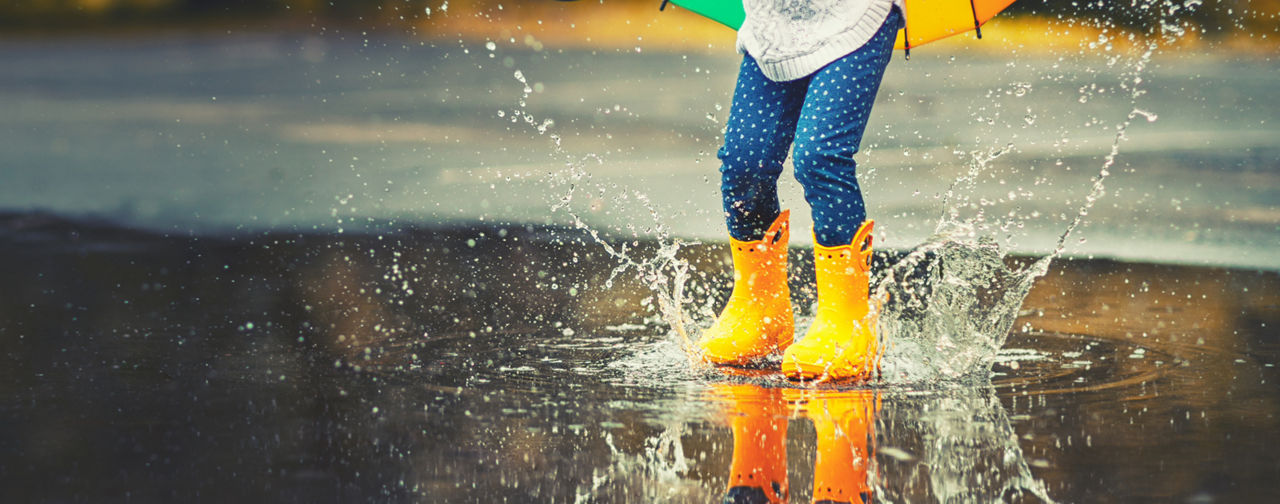child wearing yellow rain boots jumping in a puddle