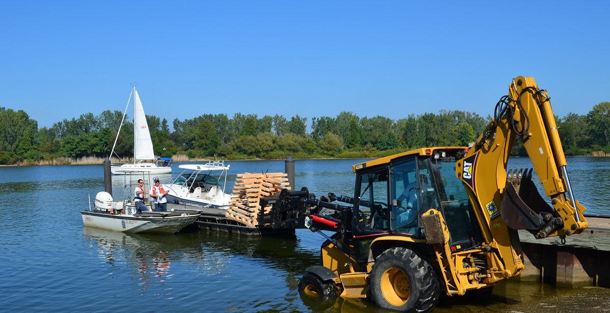 Bulldozer dropping catfish boxes into boat on lake 