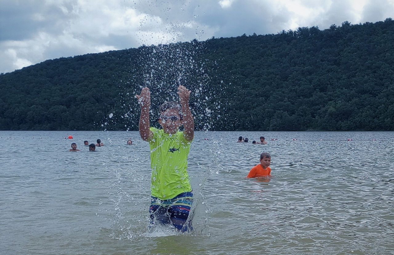 A boy splashing water in a lake with other swimmers around