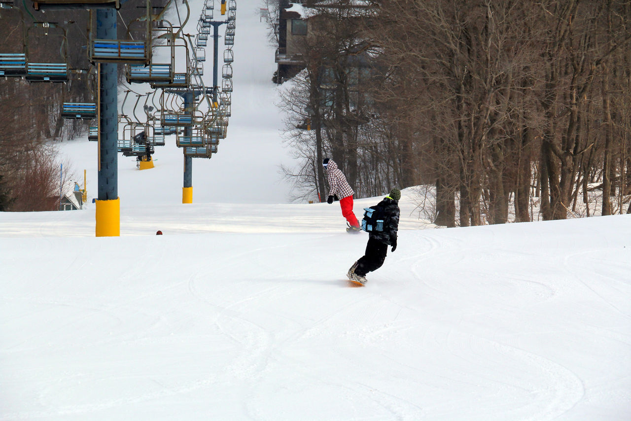 Two people snowboarding down a slope next to a ski lift