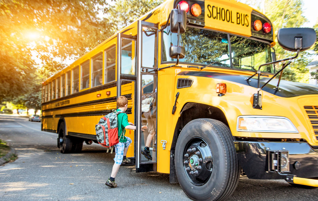 A small boy with red hair boards a school bus.