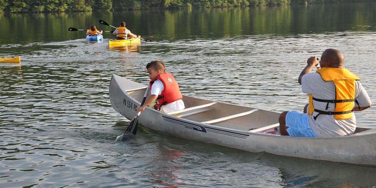 Boy and man paddle a canoe towards other paddlers in lake 