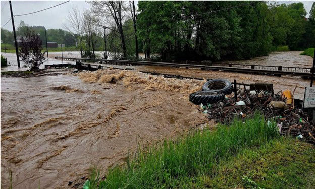 Rising waters wash over a bridge. A large pile of debris pushes up against the bridge.  