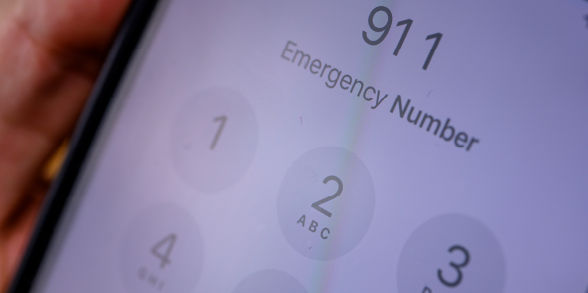 A person holds a cellphone that reads "911 emergency number" on its screen.