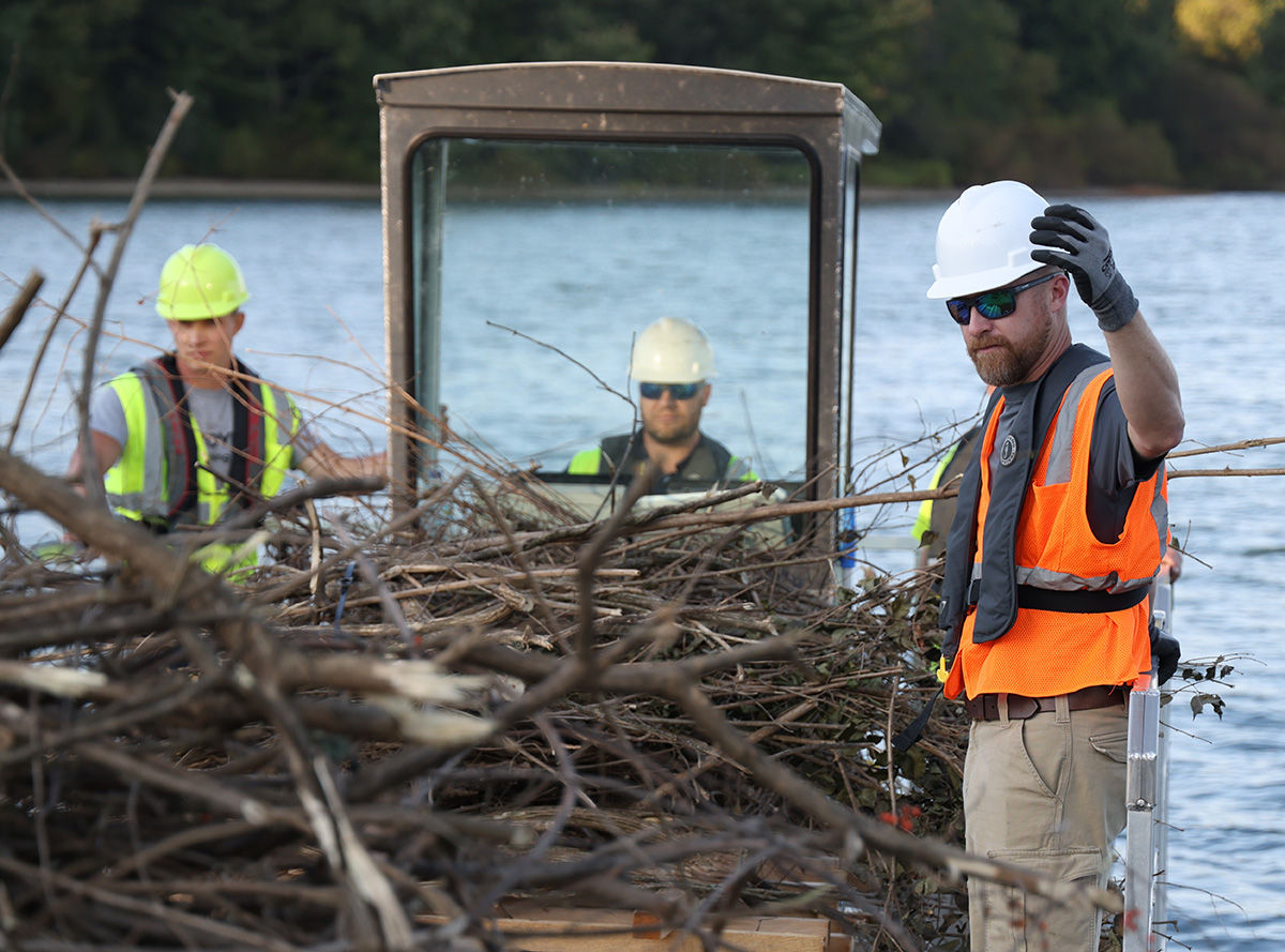 PFBC habitat biologists wearing safety gear while on a boat hauling tree brush for a lake habitat improvement project.