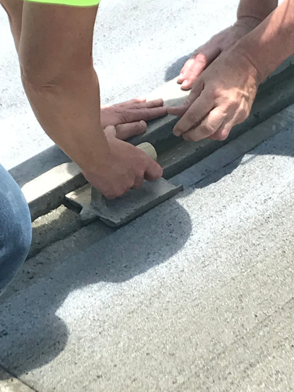 A close-up image of two hands working with a tool to finish a concrete pavement