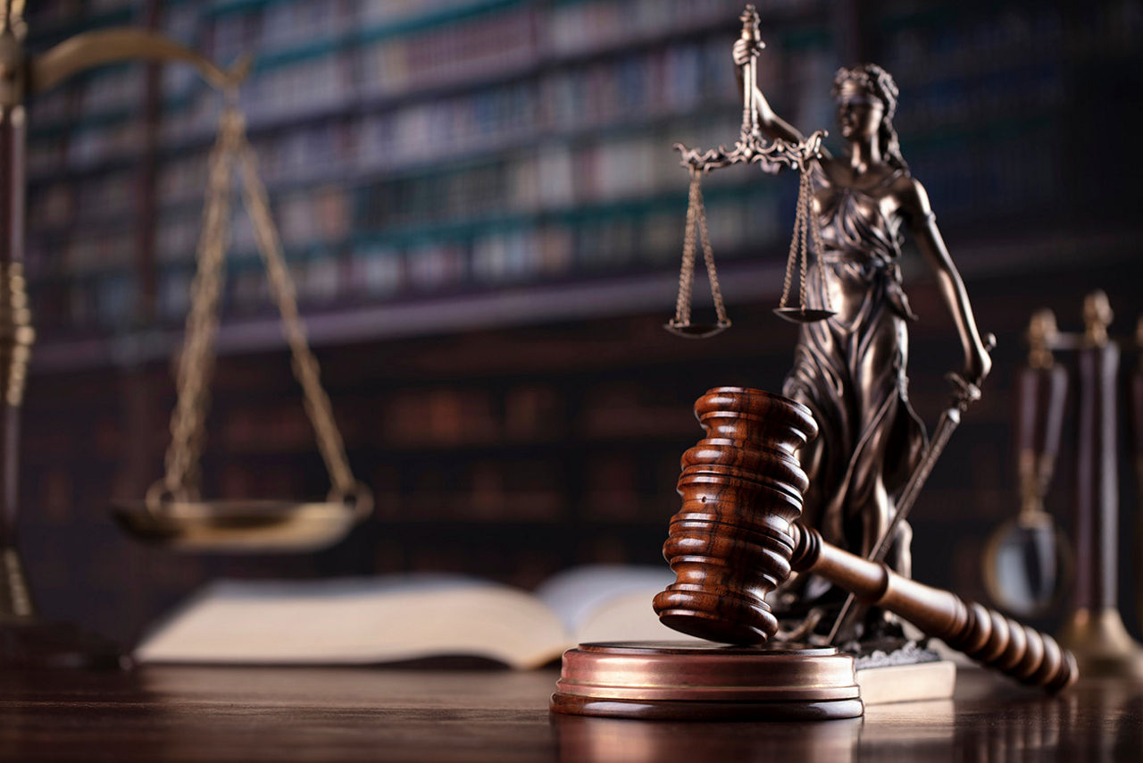 A gavel in front of a statue holding the scales of justice