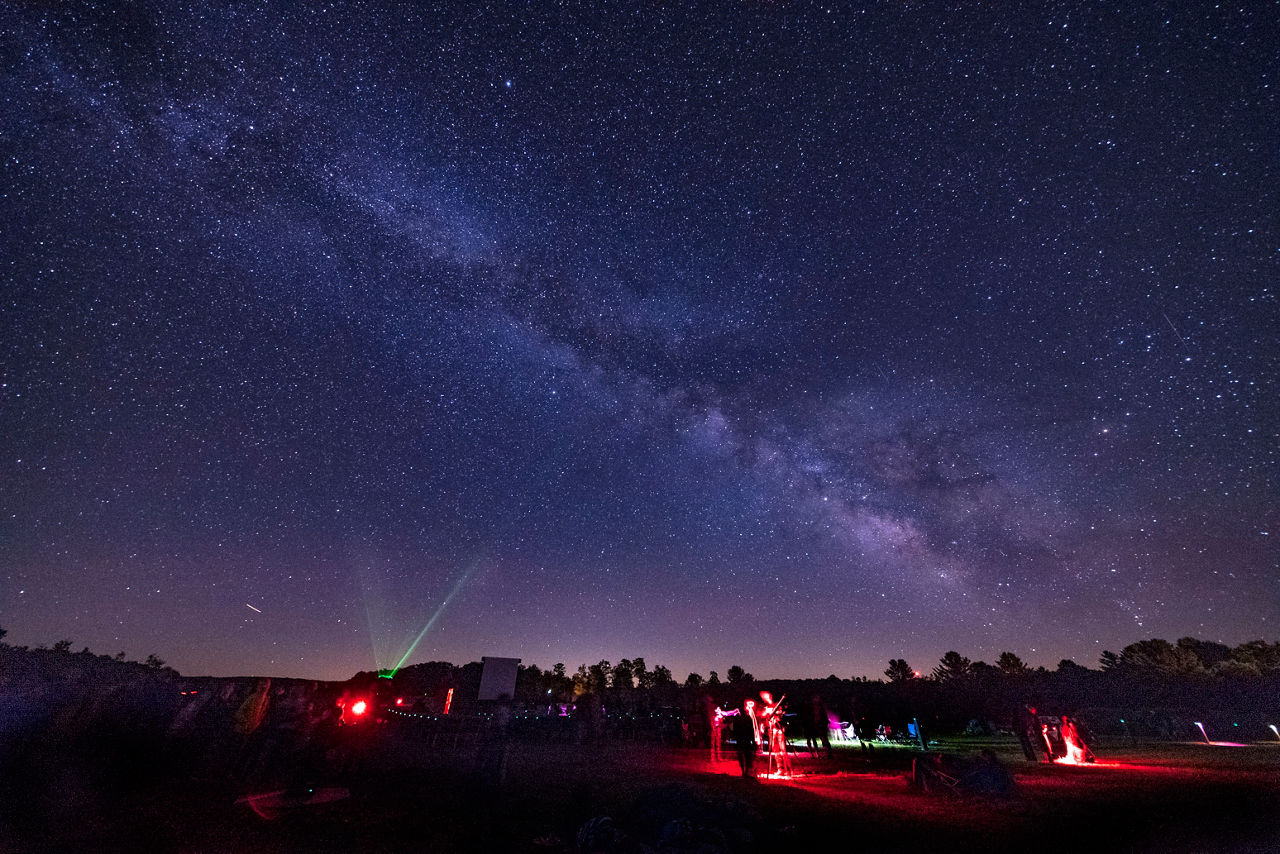 Many stargazers in a field using astronomy equipment to view a dark sky with numerous stars visible