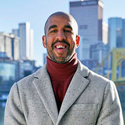 Marcus Shoffner stands outdoors for a portrait wearing a thick winter coat. A city skyline is in the distance.