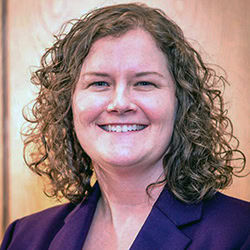 Sarah Hall smiles wearing purple suit jacket