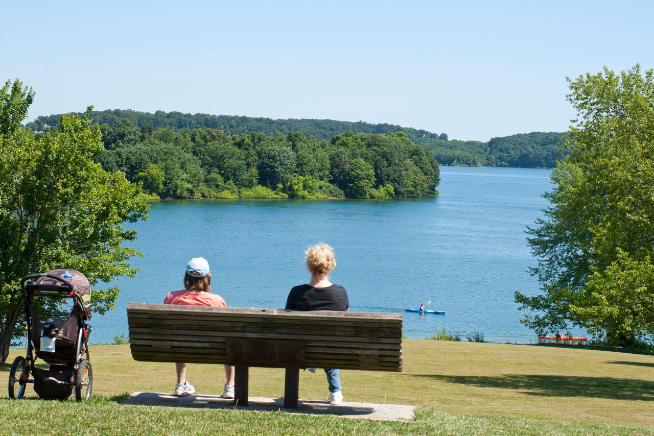 Two women sitting on a bench overlooking the lake with a kayaker on a summer day