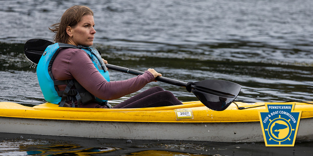 Woman wearing a properly fitting life jacket kayaking on a river. 