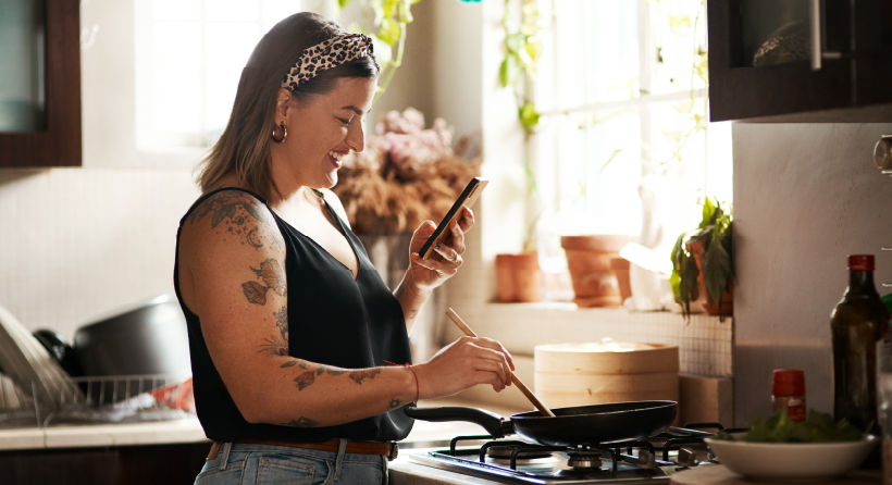 A woman is distracted by her phone while cooking.