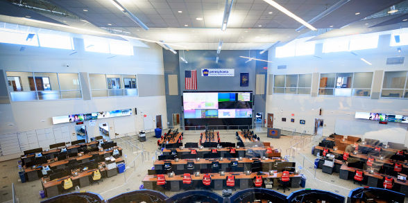 Aerial view of the Commonwealth Response Coordination Center shows lines of empty desks and chairs overlooking large screens.