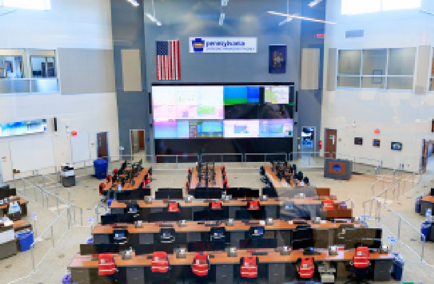 Aerial view of the Commonwealth Response Coordination Center shows lines of empty desks and chairs overlooking large screens.