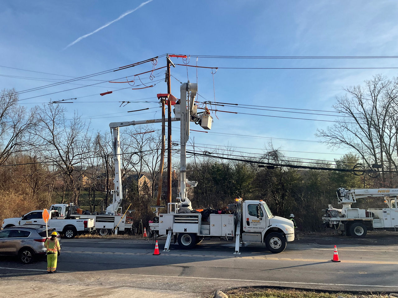 A white utility truck sits next to a two-lane roadway lined with power lines while crews make repairs.