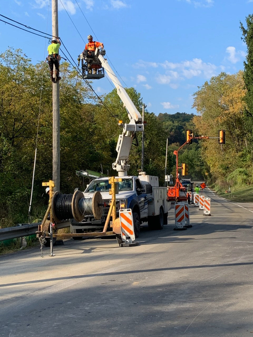 A white utility truck sits next to a two-lane roadway lined with power lines while crews make repairs.