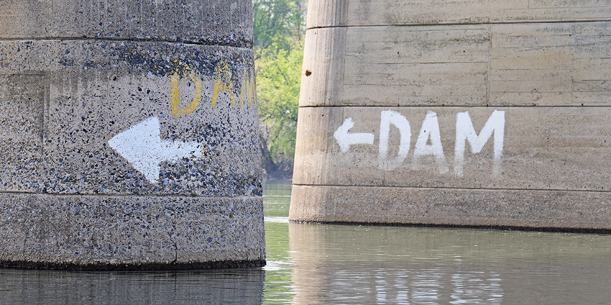 Pillar of a bridge over the Susquehanna River with "Dam" and an arrow pointing downstream to inform boaters there is a dam hazard ahead.