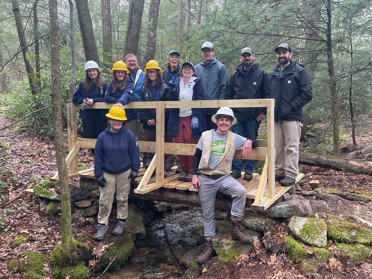 A group of PA Outdoor Corps staff pose for a photo on a newly built footbridge.