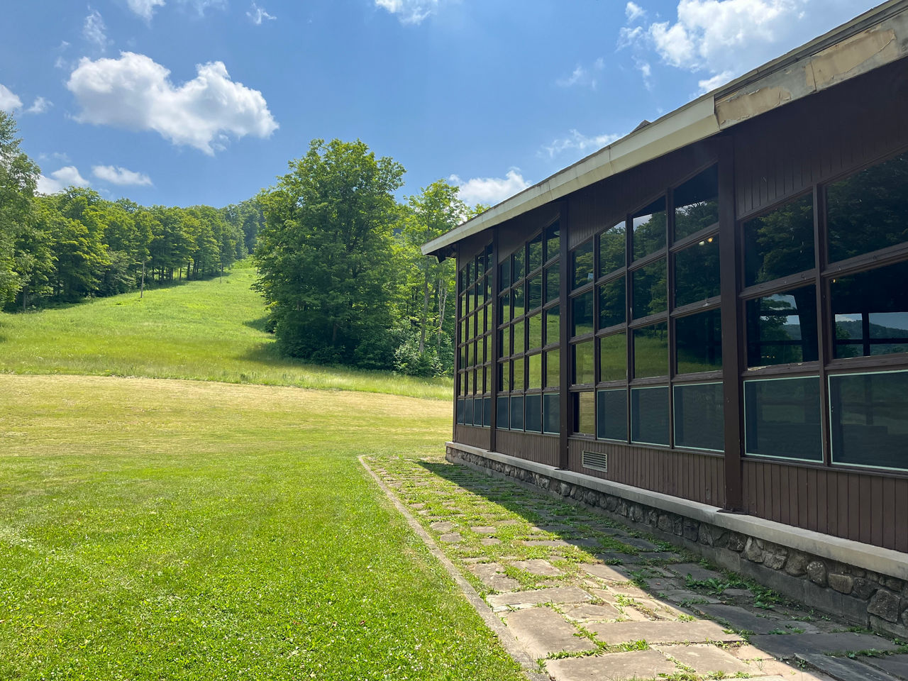 A building with many glass windows reflects the green grass and blue sky