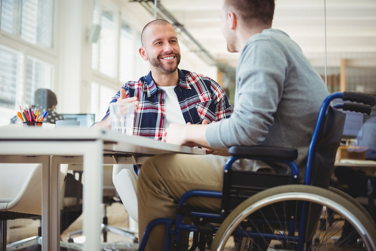 Man in wheelchair sitting with colleague in office.