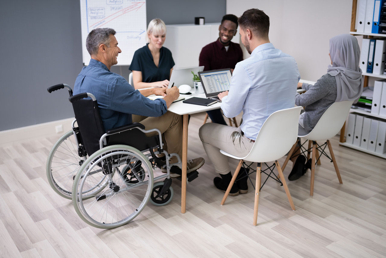 Men and women of all abilities and backgrounds gather around a table at work