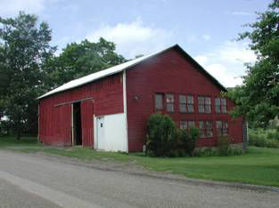 Large one story red wooden barn with sliding doors and rows of window on the gable side.